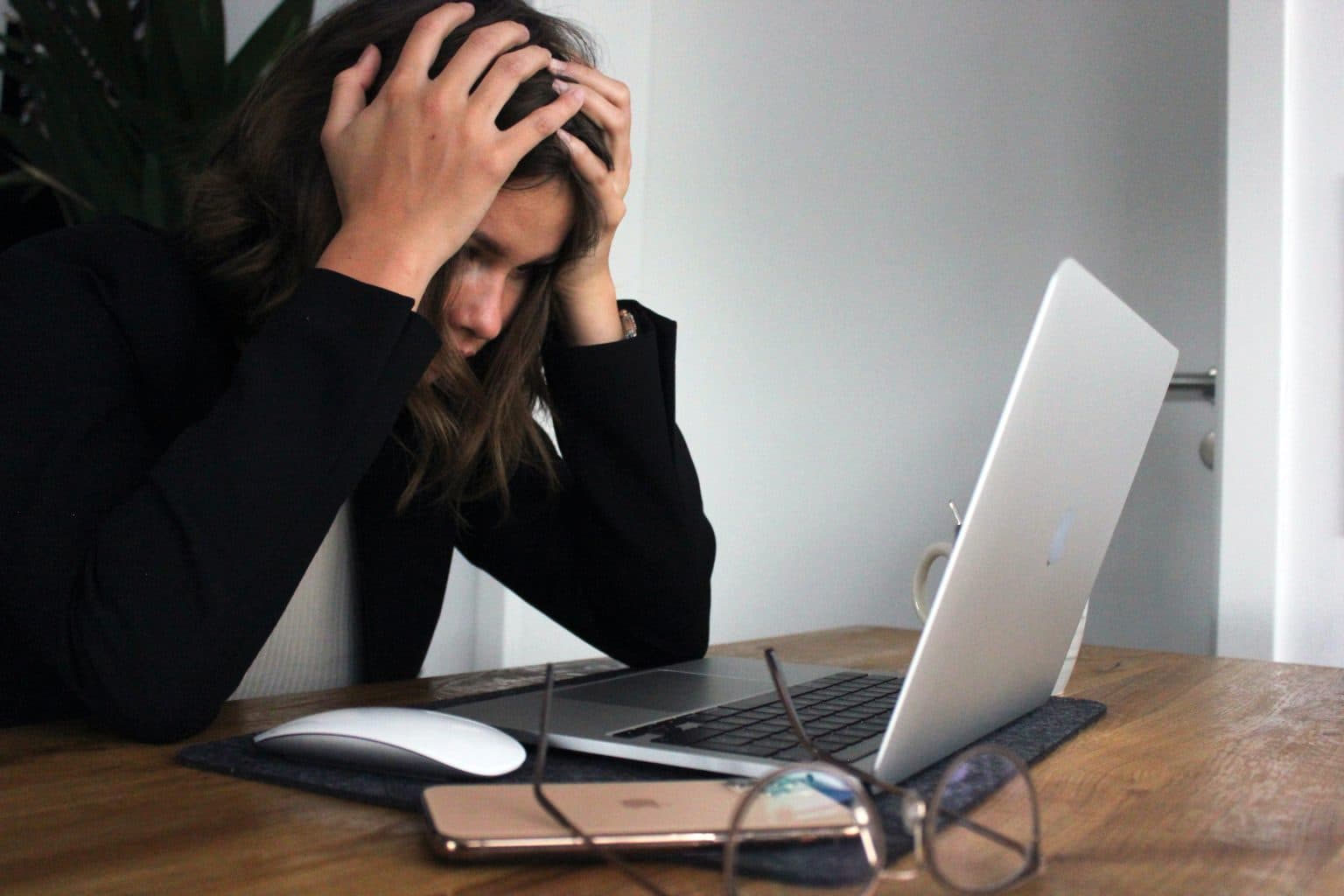 Woman sits in front of laptop with hands on head, stressed about upgrades